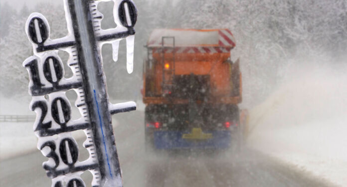 Blick auf eine vereiste Straße mit einem Lkw, der sich seinen Weg durch einen Schneesturm bahnt. Davor erkennt man ein Thermometer, welches ebenfalls mit Eis bedeckt ist. Es ist offenbar tiefster Winter und sehr kalt.