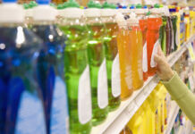 Viele verschiedene, bunte Geschirrspülmittel in Plastikverpackungen in einem Supermarktregal. Eine Hand greift zu einem der Geschirrspülmittel; der Kunde hat sich entschieden und möchte das Geschirrspülmittel kaufen.