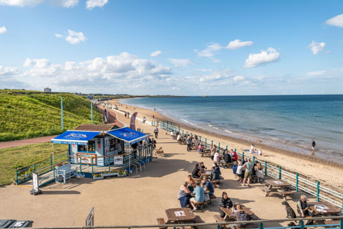 Ein Strand mit Strandhütten und Urlaubern an der Ost- oder Nordsee. Die Menschen erholen sich im Sand und entspannen sich am Wasser. Sie verbringen ihre Ferien am Meer.